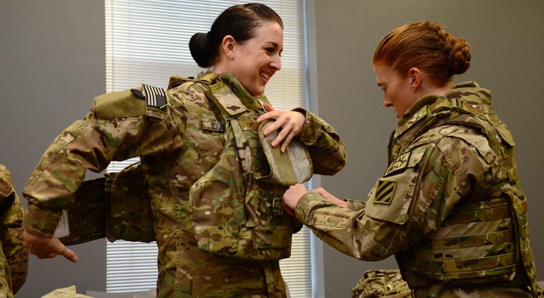 Pvt. 1st Class Cheryl Rogers grins as 2nd Lt. Chelsea Adams helps her into the new Generation III Female Improved Outer Tactical Vest, Nov. 28
