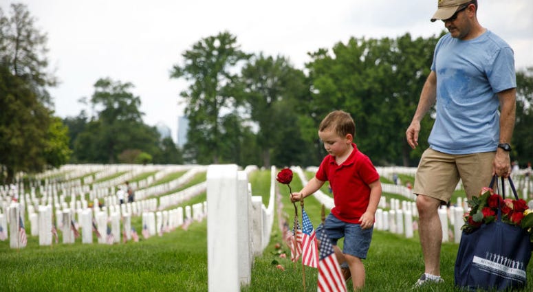 Matthew Murphy, 4, places a rose on a tombstone beside his father, Kevin Murphy, of Springfield, Virginia, during a volunteer event at Arlington National Cemetery. Memorial Day weekend across America.