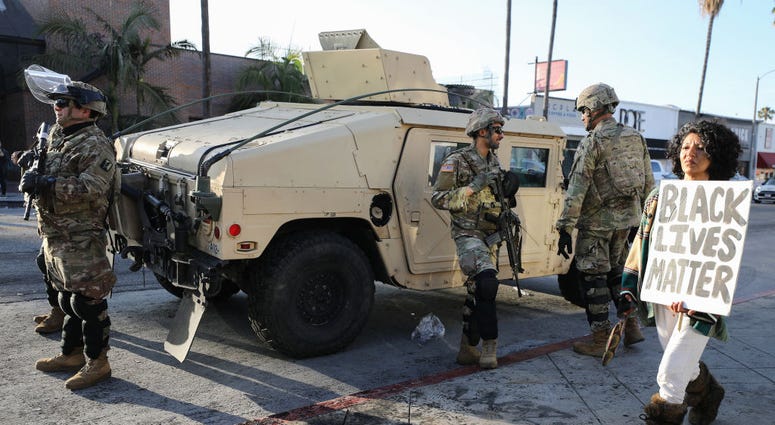 A woman carries a 'Black Lives Matter' sign past U.S. National Guard troops in the Fairfax District, an area damaged during yesterday's unrest, after the troops were activated by California Governor Gavin Newsom following violent demonstrations. A woman carries a 'Black Lives Matter' sign past U.S. National Guard troops in the Fairfax District, an area damaged during yesterday's unrest, after the troops were activated by California Governor Gavin Newsom following violent demonstrations.