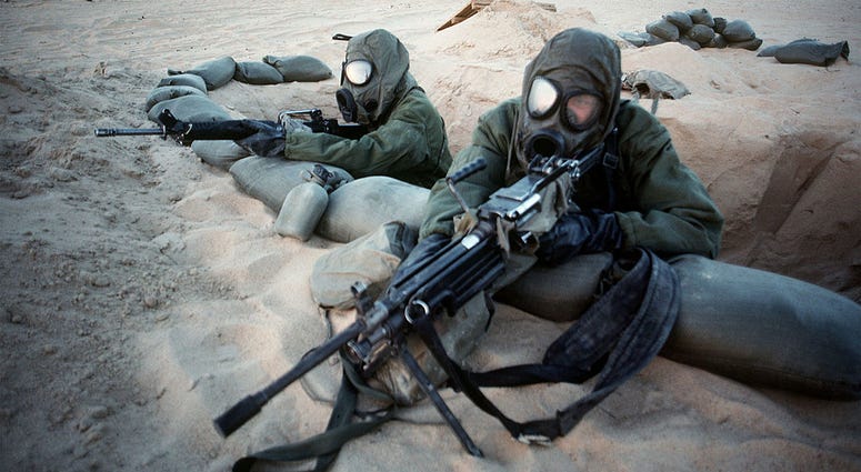 Two Marines wearing M-17A1 field protective masks man a fighting position on the perimeter of their camp while taking part in a training exercise during Operation Desert Shield. The Marine in the foreground is armed with an M-249 squad automatic weapon. GulfWarIllness2