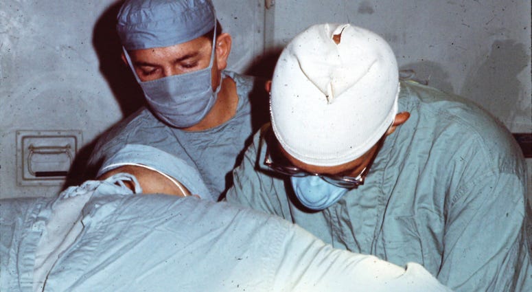On July 25, 1969, Army Surgeons Mo Levine (center) and Al Agudelo (right) operate on Specialist 5 John Fogle— shortly after John was wounded while serving as a helicopter door gunner near Phu Bai, Vietnam. Medic Mickey Caskey (foreground) assists.