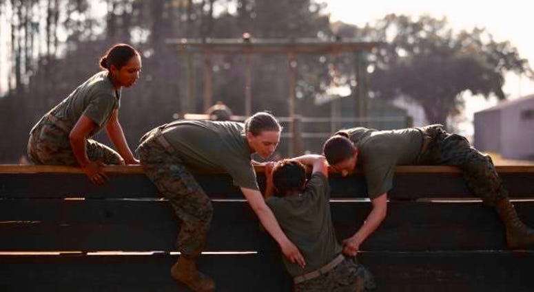 Women undergoing Marine Corps recruit training at Parris Island, South Carolina help each other make their way through an obstacle course.