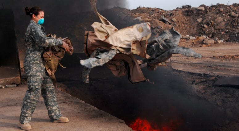 Senior Airman Frances Gavalis, 332nd Expeditionary Logistics Readiness Squadron equipment manager, tosses unserviceable uniform items into a burn pit here, March 10, 2008. BurnPits2