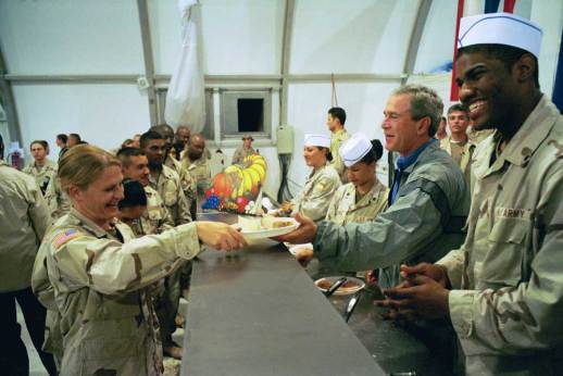 George W. Bush helps to serve Thanksgiving dinner at the Bob Hope Dining Facility, Baghdad International Airport, Iraq, during a surprise visit with troops. November 27, 2003