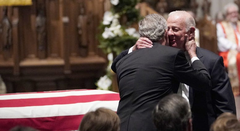 Former President George W. Bush embraces former Secretary of State James Baker after he eulogizes Bush's father, George H.W. Bush.