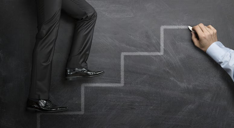 Businessman climbing the career steps drawn on a black chalkboard