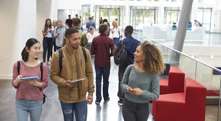 Students holding tablets and phone talk in university lobby