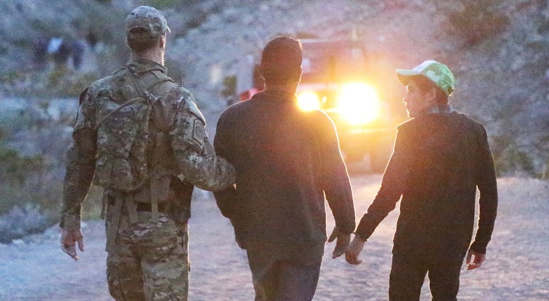 A U.S. Border Patrol agent escorts two handcuffed young men down the trail to Mount Cristo Rey during the Good Friday pilgrimage near Sunland Park, N.M. April 14, 2017.