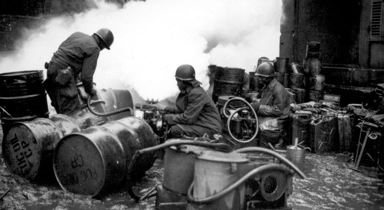 11. Soldiers of the 161st Chemical Smoke Generating Company, U.S. Third Army, move a barrel of oil in preparation to refilling an M-2 smoke generator. These men are laying a smoke screen to cover bridge building activities.