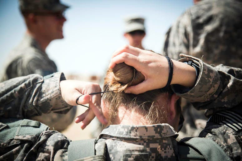 Spc. Nina Bray, intelligence analyst, Headquarters and Headquarters Company, 204th Brigade Support Battalion, 2nd Armored Brigade Combat Team, 4th Infantry Division, fixes her hair bun before putting on her body armor at a M203/M320 40 mm grenade launcher