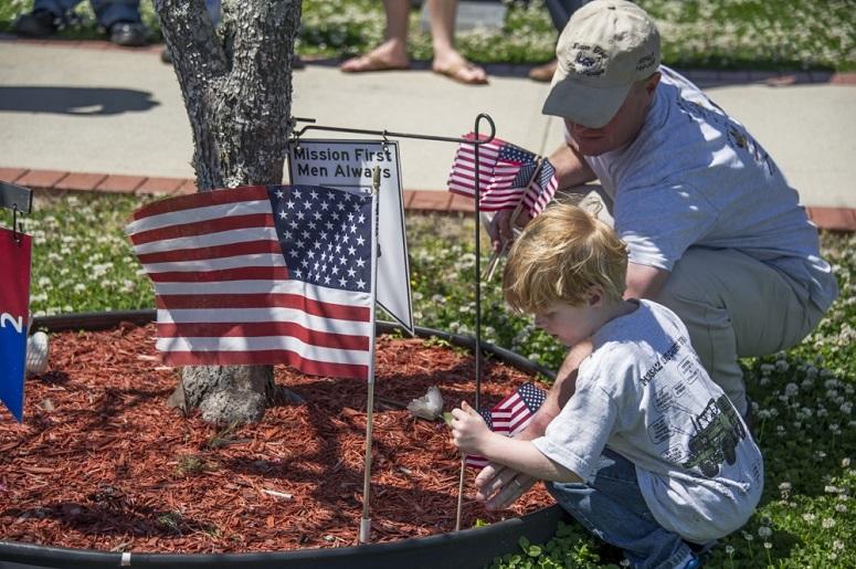 U.S. Army Sgt. Joseph Carson, and his son plant a flag at the base of a memorial tree for Staff Sgt. Stevon Booker, a tank commander with Alpha Company, 1st Battalion, 64th Armor Regiment, 2nd Brigade Combat Team, 3rd Infantry Division, at Fort Stewart, G