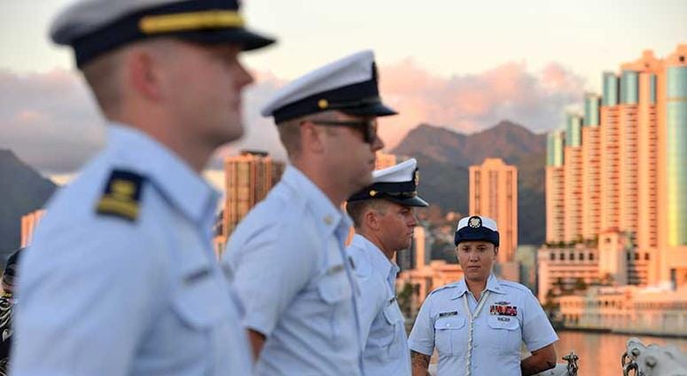 Coast Guard Cutter Sherman crewmembers line the rail of the flight deck prior to evening colors during a ceremony aboard the Sherman the night before the cutter is scheduled to be decommissioned in Honolulu, Mar. 28, 2018. Launched in September 1968, Sher