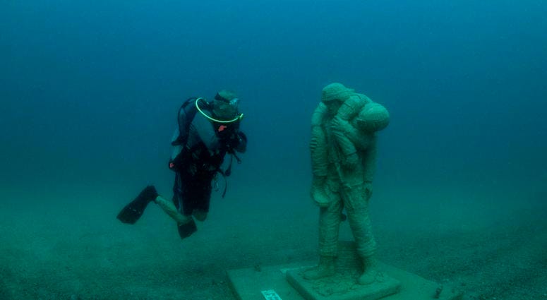 A diver comes face-to-face with one of 12 life-size statues of members of the Armed Forces that make up the Circle of Heroes underwater veterans memorial. DiverStatue