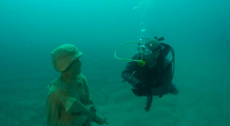 A diver comes face-to-face with one of 12 life-size statues of members of the Armed Forces that make up the Circle of Heroes underwater veterans memorial. DiverStatue