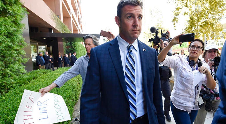 U.S. Rep. Duncan Hunter, center, leaves an arraignment hearing as a protester carries a sign, left, Thursday, Aug. 23, 2018, in San Diego. Hunter and his wife Margaret pleaded not guilty Thursday to charges they illegally used his campaign account for per