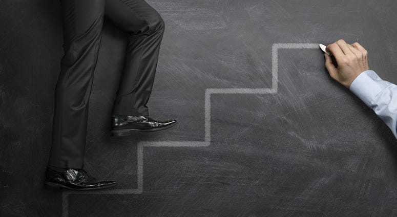 Businessman climbing the career steps drawn on a black chalkboard