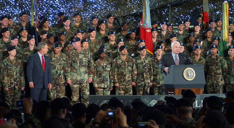 June 18, 2004: Sen. John McCain, R-Az., prepares to speak to a gathering of service members and their families at Fort Lewis, Wa. President George W. Bush converses with several soldiers on stage.