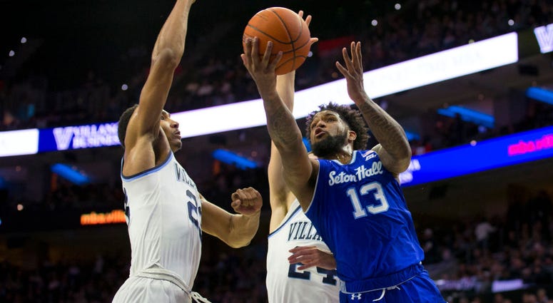 A Seton Hall player goes up for a shot while being guarded by to Villanova players.