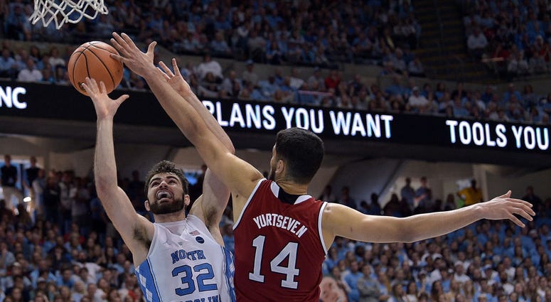 Photo of an NC State player attempting to block a North Carolina player's shot.