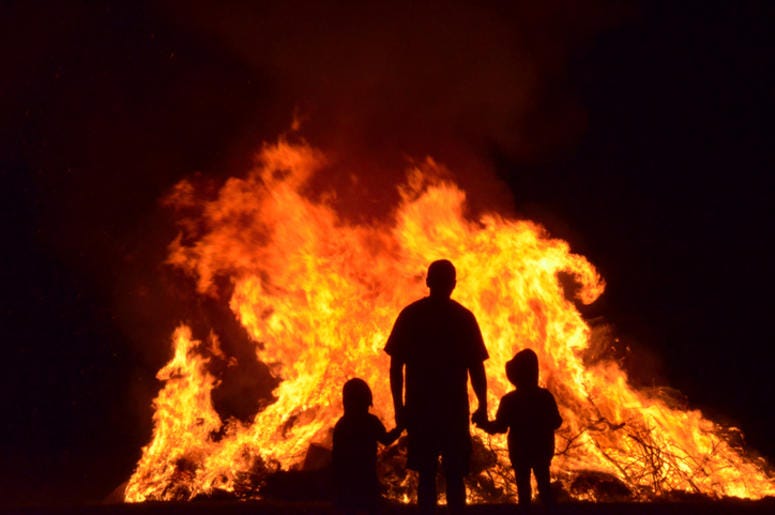 Man and children in silhouette watching the flames of a huge b