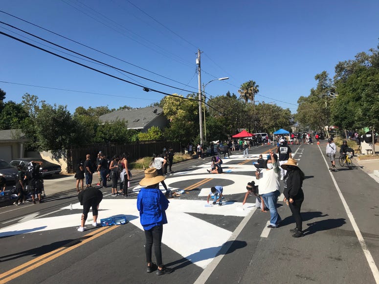 Activists paint large letters in white on a street in San Jose.