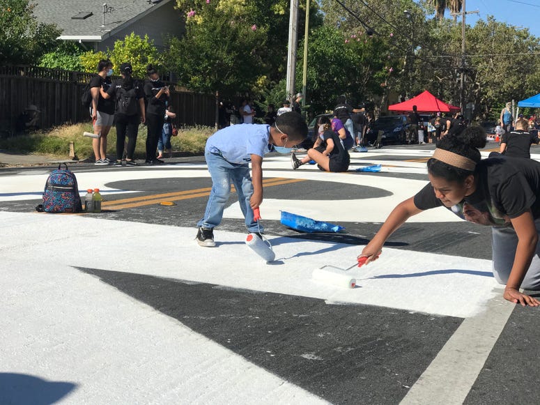 Activists paint large letters in white on a street in San Jose.