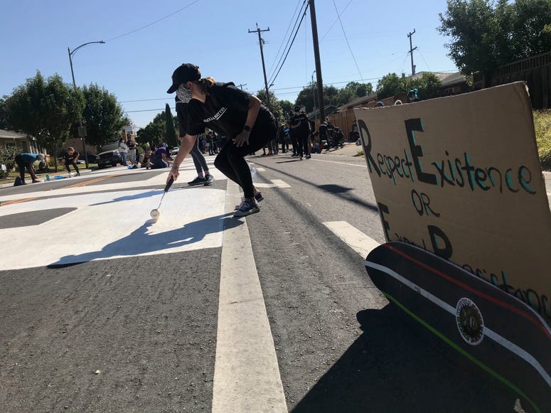 Activists paint large letters in white on a street in San Jose.