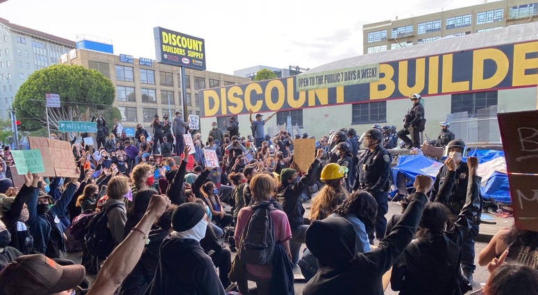 Protestors blocking 13th St. under the freeway in San Francisco kneeling in front of police.