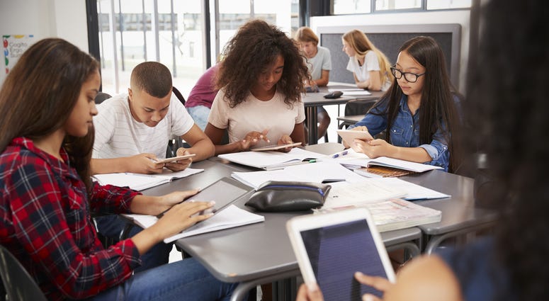 Teacher sitting with high school students using tablets Teacher sitting with high school students using tablets