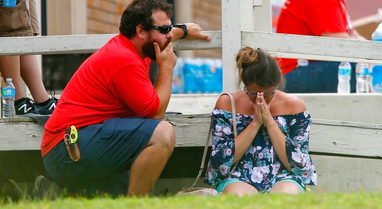 A woman prays in the grass outside the Alamo Gym where parents wait to reunite with their kids following a shooting at Santa Fe High School Friday, DO NOT USE