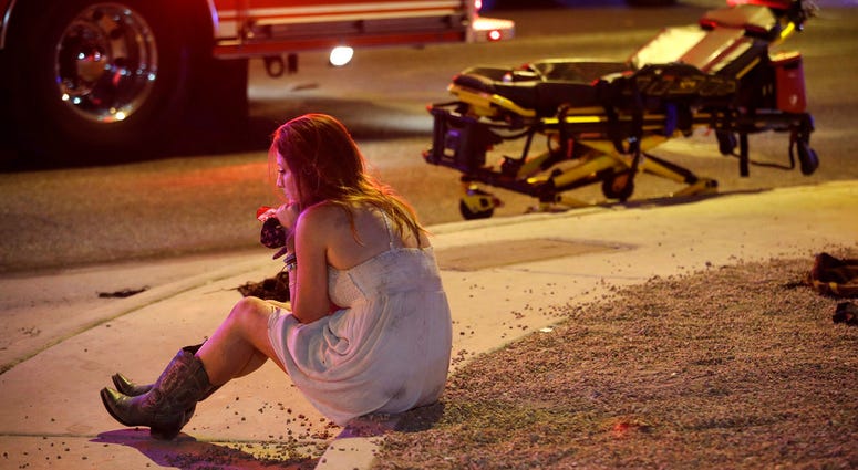 In this Oct. 2, 2017 file photo, a woman sits on a curb at the scene of a shooting outside a music festival on the Las Vegas Strip. DO NOT USE