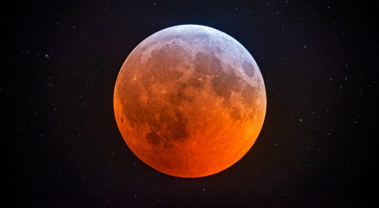 The totally eclipsed moon glows with a reddish color against the background stars The totally eclipsed moon glows with a reddish color against the background stars