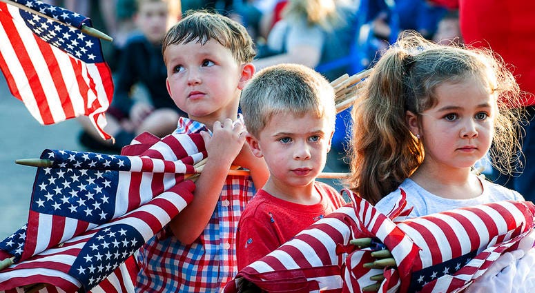 Brayden Austin, left, Gavin Colby, middle, and Brylee Roberge patiently wait with an armful of flags to be burned at Veterans Memorial Park in Lewiston, Maine DO NOT USE