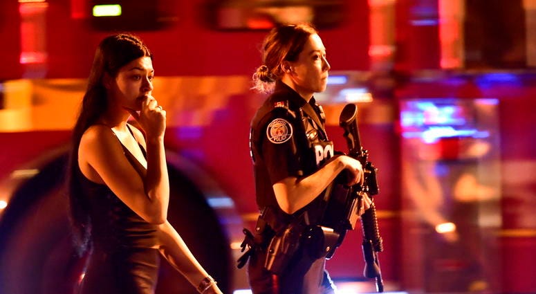 A police officer escorts a civilian away from the scene of a shooting, Sunday, July 22, 2018, in Toronto. DO NOT USE