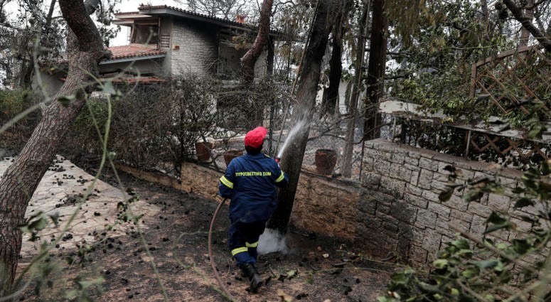 A fireman sprays water outside a burnt house at Kineta village, west of Athens, Tuesday, July 24, 2018. DO NOT USE