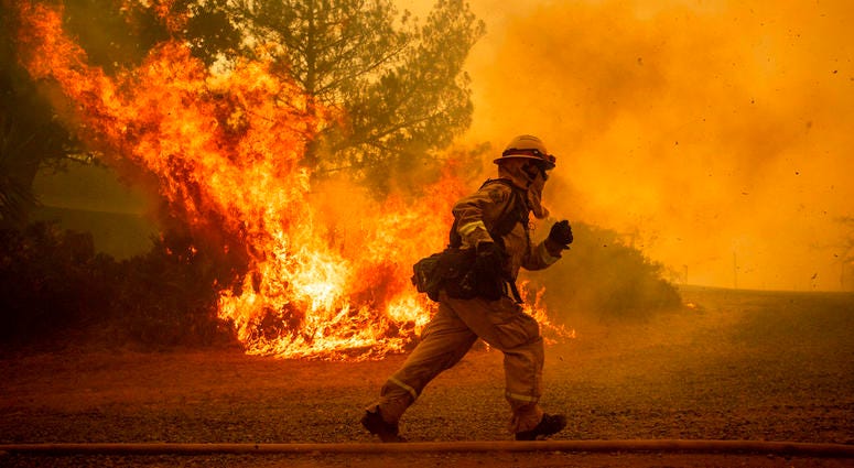 A firefighter runs while trying to save a home as a wildfire tears through Lakeport, Calif
