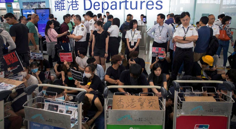 Airport security personnel stand guard as travelers walk past protesters holding a sit-in rally at the departure gate of the Hong Kong International Airport in Hong Kong, Tuesday, Aug. 13, 2019. AP DO NOT USE