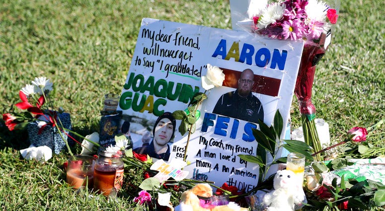 tribute to student Joaquin Oliver and coach Aaron Feis is left at the base of a white cross at Pine Trails Park in Parkland, Fla. DO NOT USE