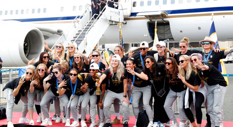 Members of the United States women's soccer team, winners of a fourth Women's World Cup, celebrate and pose with the trophy by their plane after arriving at Newark Liberty International Airport, Monday, July 8, 2019, in Newark, N.J.
