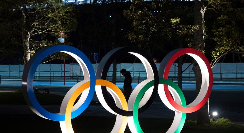 A man is seen through the Olympic rings in front of the New National Stadium in Tokyo, Tuesday, March 24, 2020. IOC President Thomas Bach has agreed "100%" to a proposal of postponing the Tokyo Olympics for about one year until 2021 because of the coronav