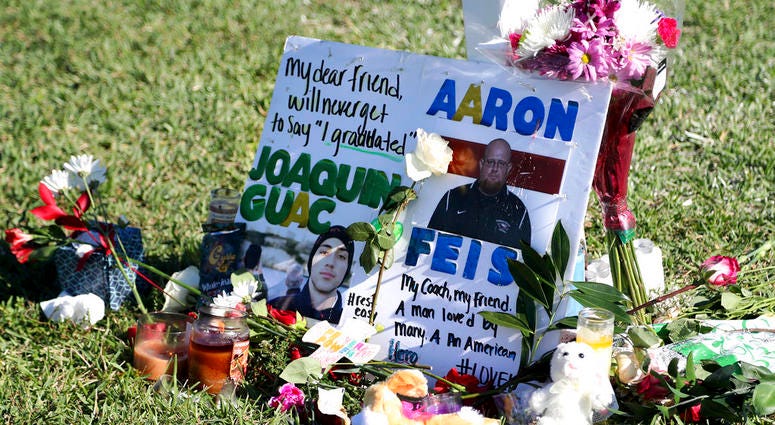 tribute to student Joaquin Oliver and coach Aaron Feis is left at the base of a white cross at Pine Trails Park in Parkland, Fla. DO NOT USE