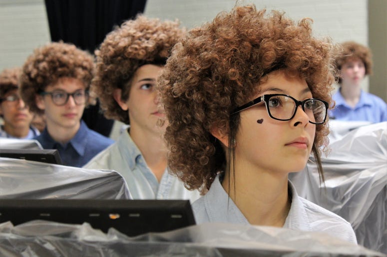 Ariceli, wearing her Bob Ross wig, listens to the artist speak on a video screen before painting began Thursday at Madison Middle School on Flash Bob Flash Mob Day.