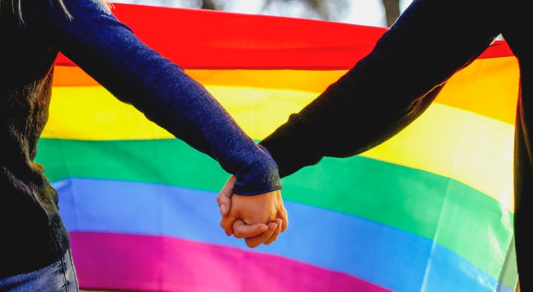 lgbtq couple holding hands in front of rainbow flag