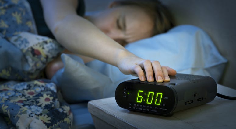 Young woman pressing snooze button on early morning digital alarm clock radio Young woman pressing snooze button on early morning digital alarm clock radio