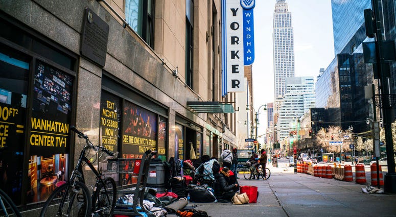 homeless people camping on a sidewalk, empire state building in the background