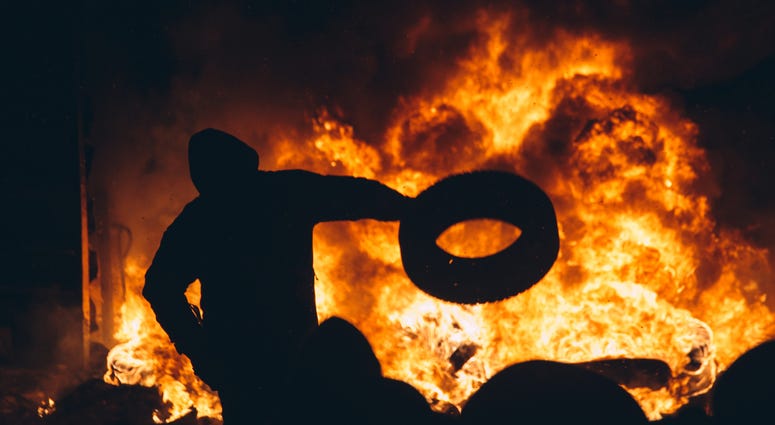 rioters fueling a fire with a tire