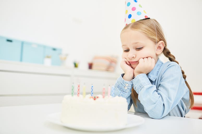 Sad birthday - Sad little girl in birthday cap looking at festive cake with candles Sad birthday - Sad little girl in birthday cap looking at festive cake with candles