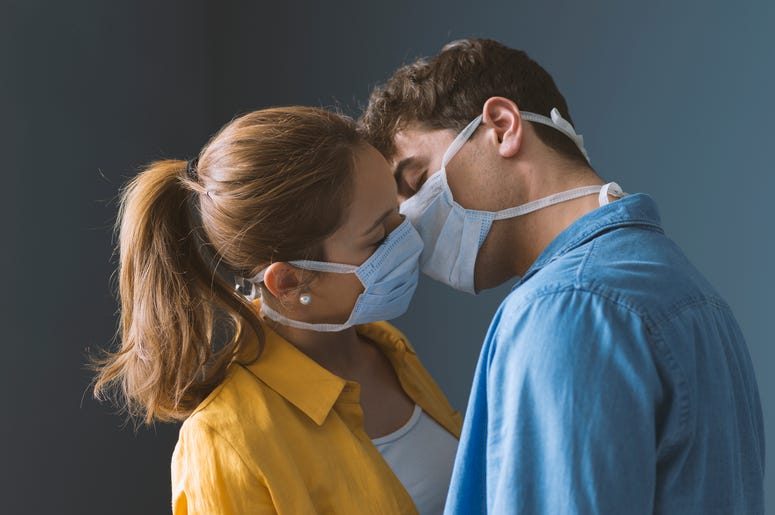 (cyano66/ iStock/ Getty Images Plus) Young couple wearing protective face masks and kissing each other, virus spread prevention