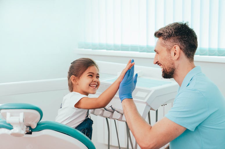 Laughing little girl high fives dentist at dental clinic Laughing little girl high fives dentist at dental clinic