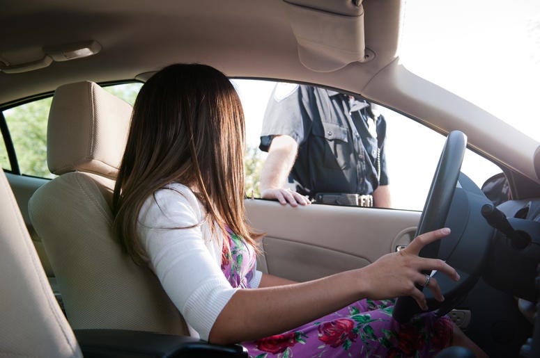 (bmcent1/ iStock/ Getty Images Plus) Police officer has just pulled over a brunette woman and approaches her car.